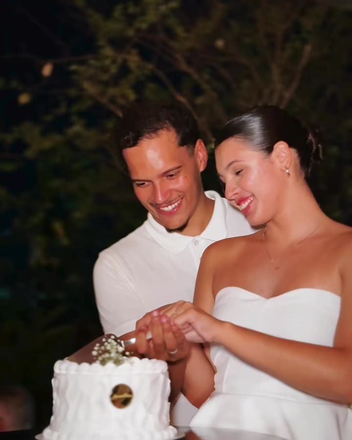 Casal de noivos cortando juntos um bolo branco Amantícia