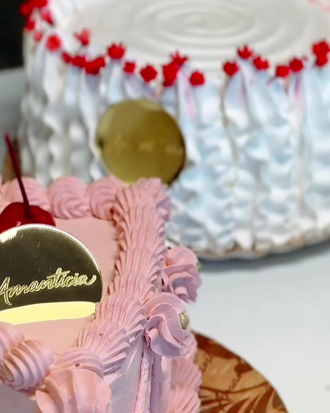 Bolos personalizados Amantícia: um rosa com bicos de confeitar e cereja e outro branco com detalhes vermelhos, ambos com a placa dourada da marca