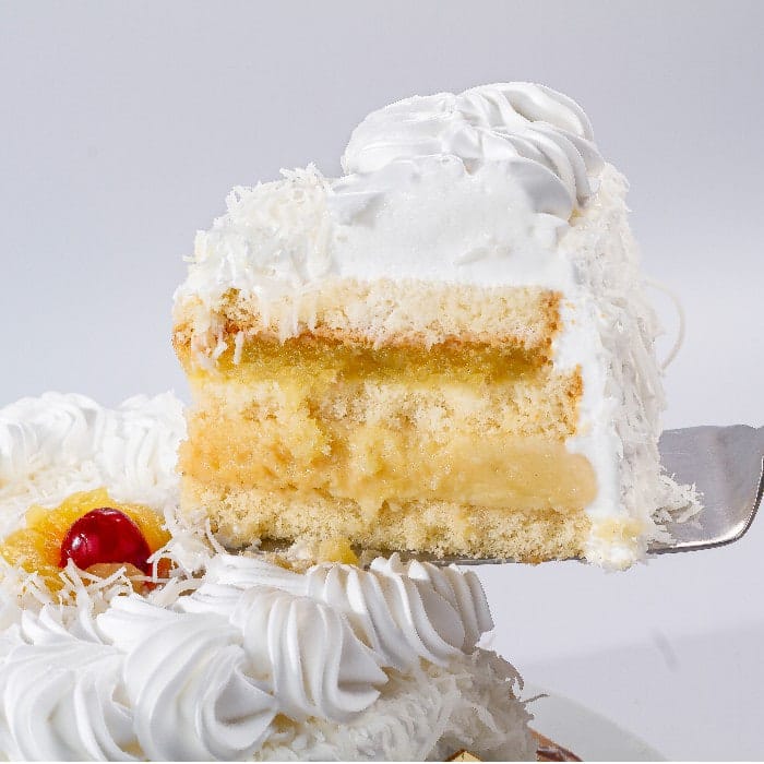 Fatia de Bolo Abacaxi com Coco com recheio cremoso e cobertura de chantilly e flocos de coco
